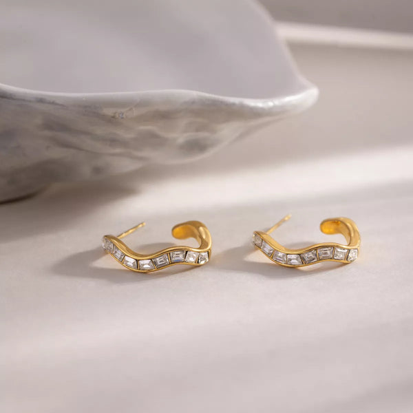 Pair of gold-tone zircon hoop earrings shown flat on a pale surface