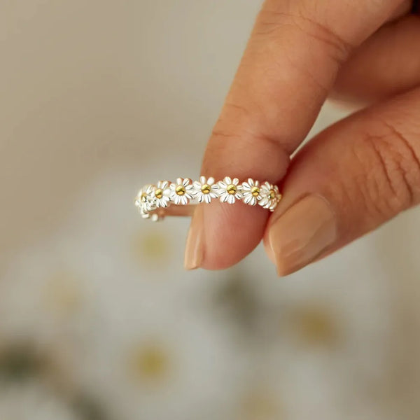 Gold-tone band ring with small flower-shaped stones held between fingers
