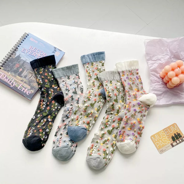 Five sheer crew socks with floral prints in dark, gray, blue and cream colorways
