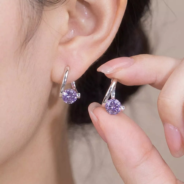 Silver-tone hoop earrings with purple round stones held beside an ear