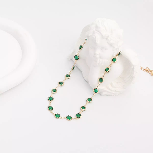 Gold-tone necklace with oval dark green rhinestones arranged on a white display