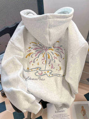 Light grey hoodie draped over a chair, showing the hood and pastel fireworks graphic on the back