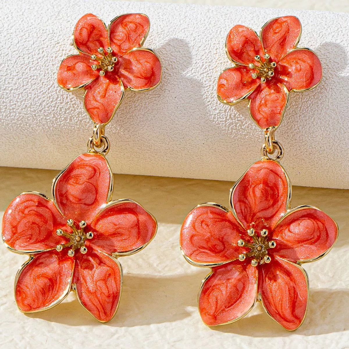 Orange-red double-flower dangle earrings displayed upright against a light background.
