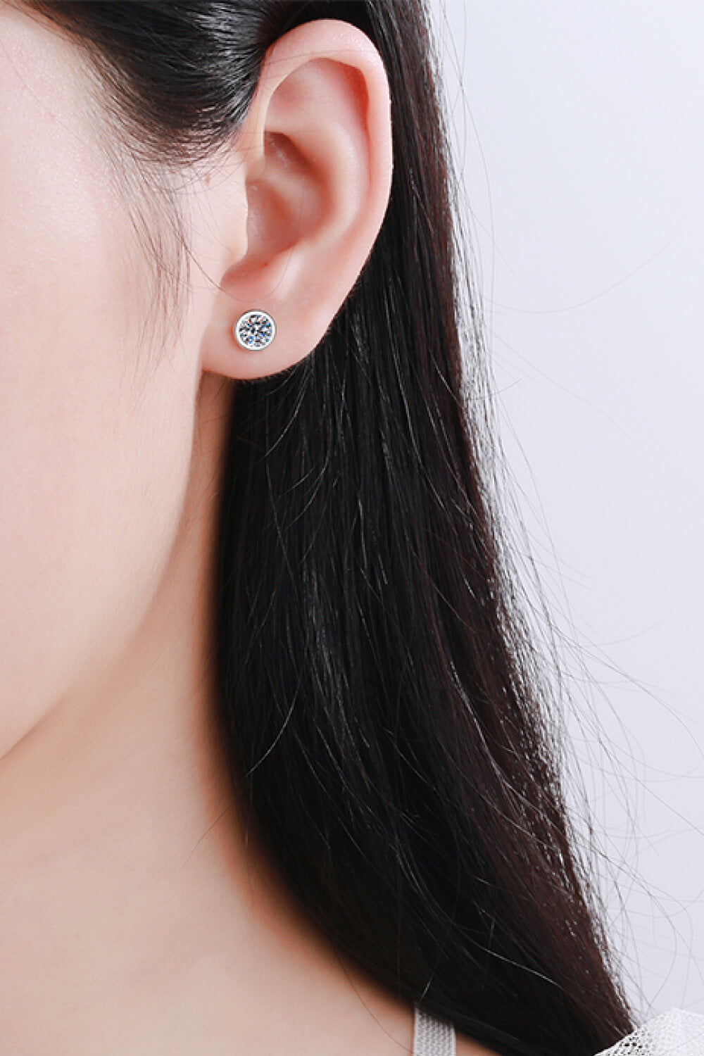 Round clear-stone stud earrings worn on an ear