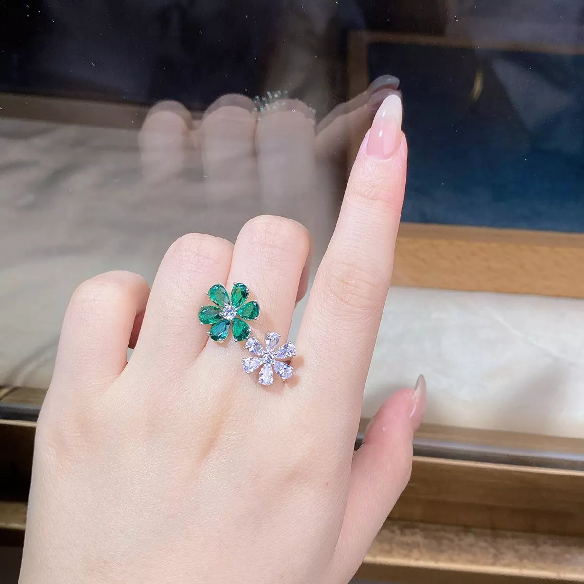 Green jeweled flower ring with a clear flower accent worn on a hand