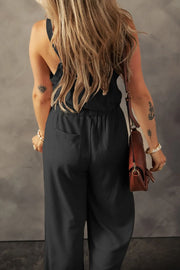 Black textured jumpsuit with knotted straps, model back view with shoulder bag