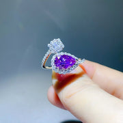 Purple teardrop moissanite bypass ring with a round halo detail, held between fingers