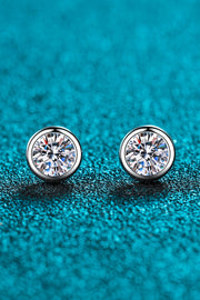 Pair of round clear-stone stud earrings with silver-tone bezels on teal surface