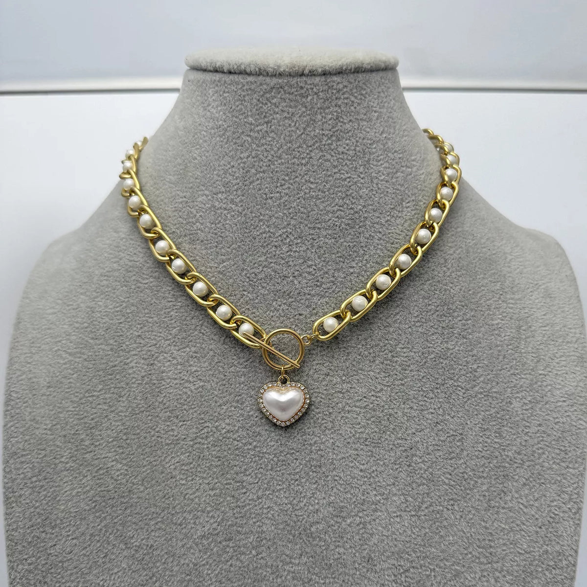 Chunky pearl and heart pendant necklace displayed on a grey bust