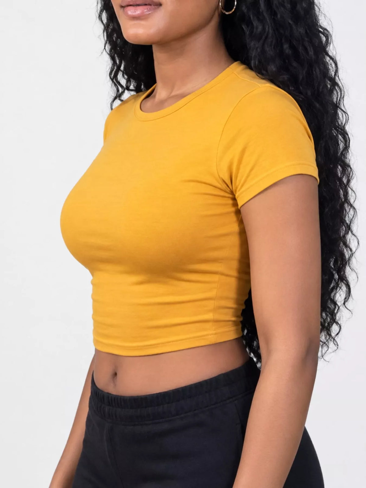 Golden yellow crew-neck crop T-shirt worn with dark pants, side view.