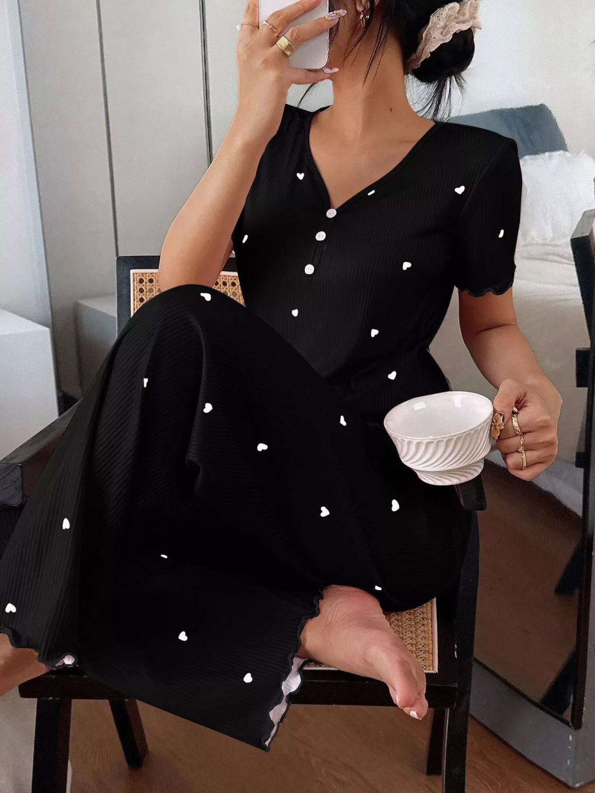 Seated model in black heart-print lounge set holding a cup with one knee raised