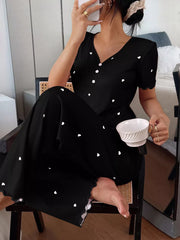 Seated model in black heart-print lounge set holding a cup with one knee raised