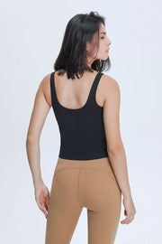 Front view of a woman wearing a black V-neck fitted tank with tan leggings.