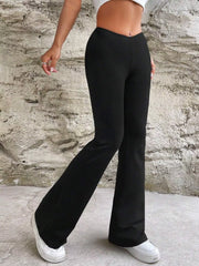 Side view of black flare pants showing the fitted thigh and flared hem over white trainers.