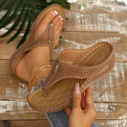 Taupe perforated toe-post wedge sandal held to show the side and footbed