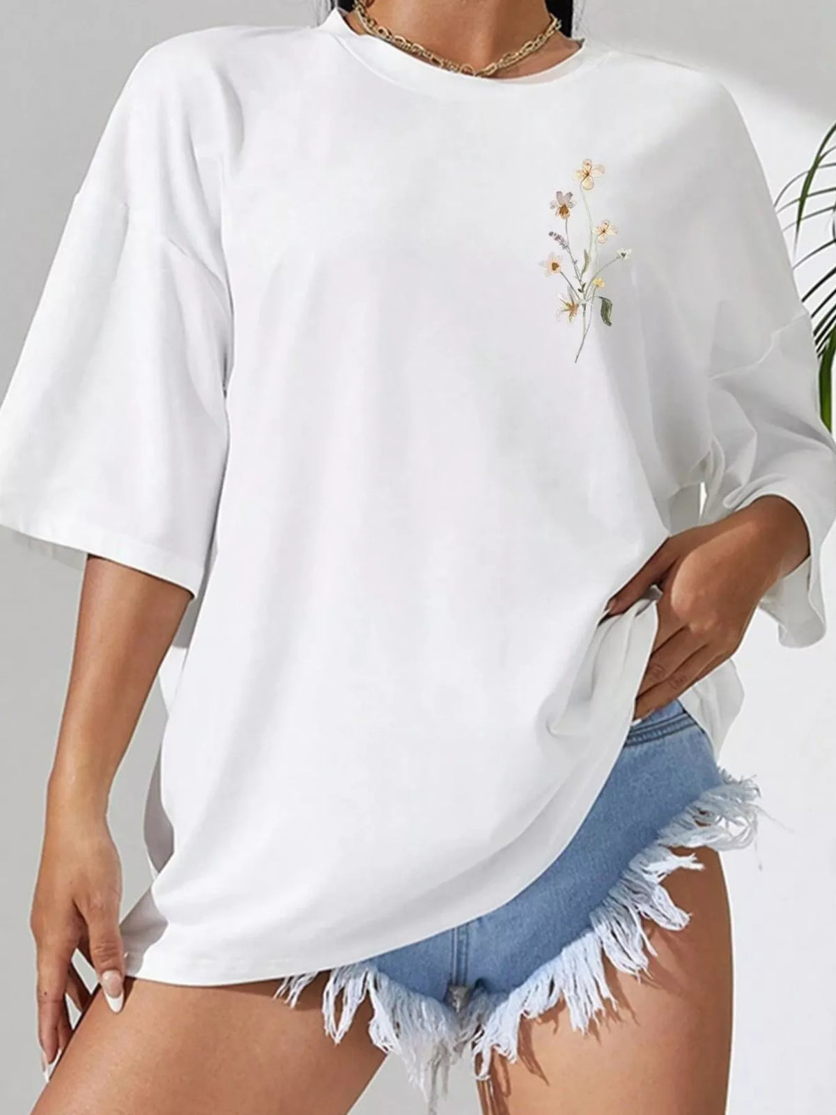 Front view of white oversized tee with small floral chest motif and denim shorts