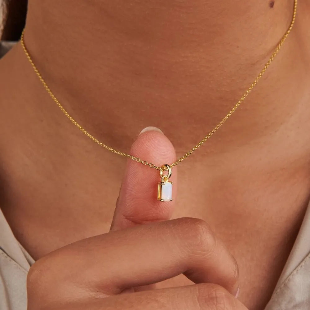 Close-up of a model holding a white rectangular pendant on a gold-tone chain