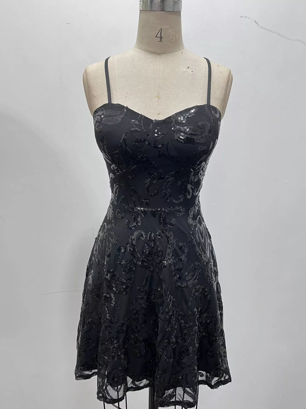 Black floral-sequin mini dress displayed on a dress form against a pale wall.