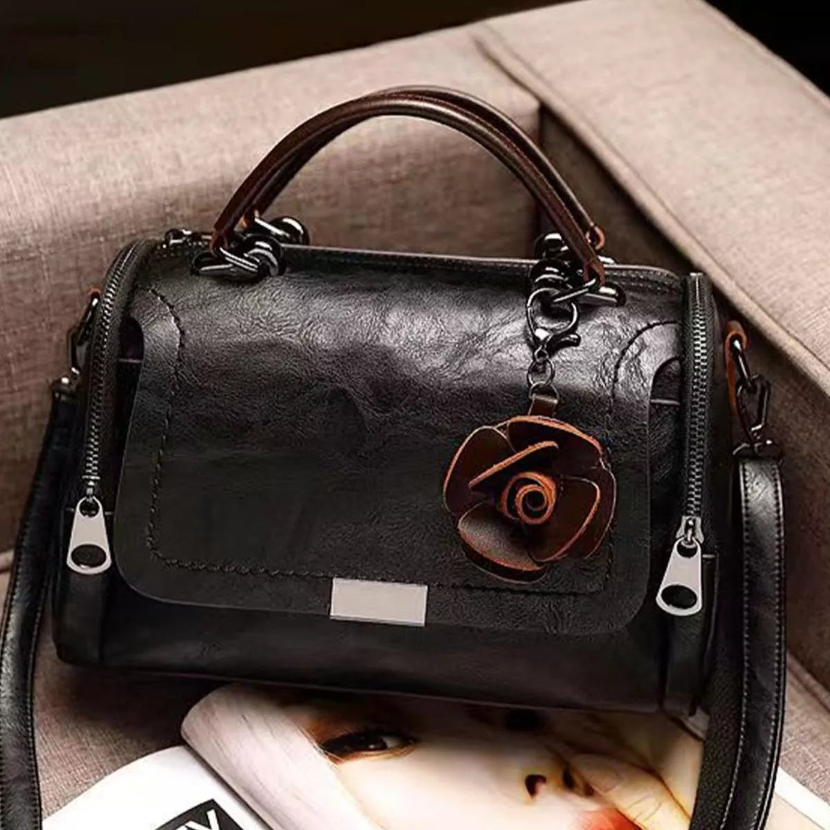 Front view of black flap crossbody bag with flower ornament and twin handles