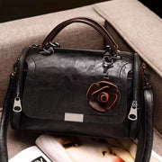Front view of black flap crossbody bag with flower ornament and twin handles
