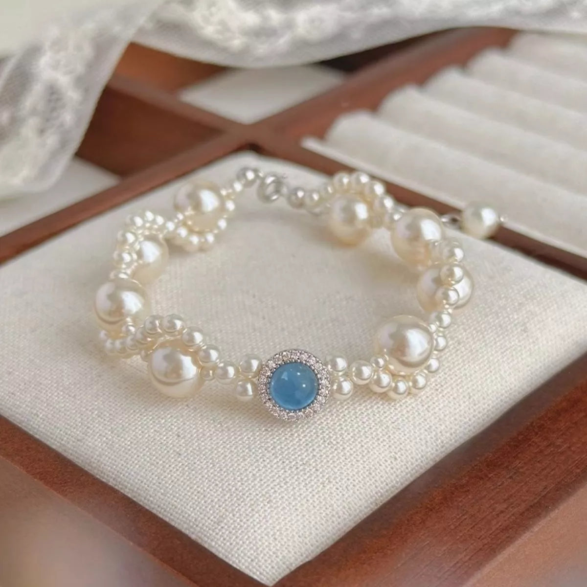 Pearl bracelet with blue center stone displayed on a cushion