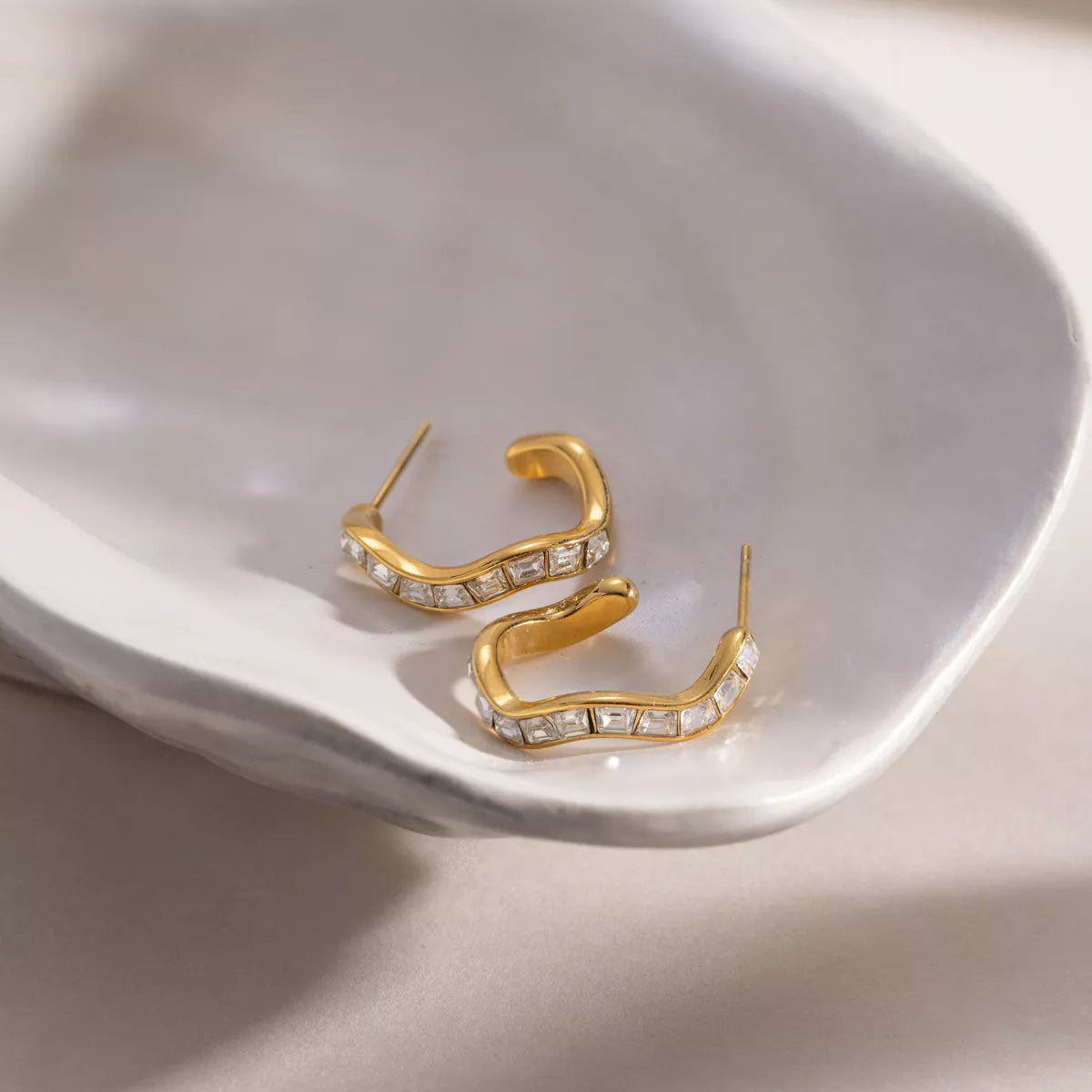 Gold-tone zircon hoop earrings resting inside a ceramic dish
