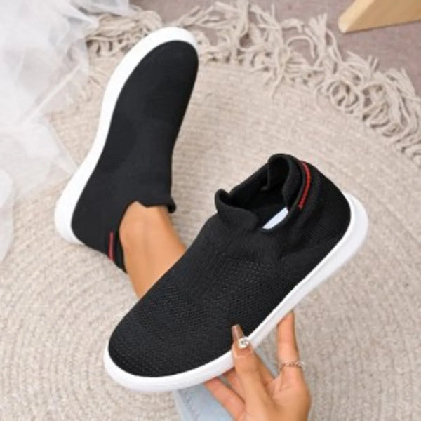 Black knit slip-on shoe held beside a matching shoe worn on a foot