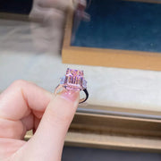 Rectangular pink gemstone ring held between fingers, showing the raised setting
