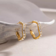 Gold-tone zircon hoop earrings displayed upright on a ceramic dish