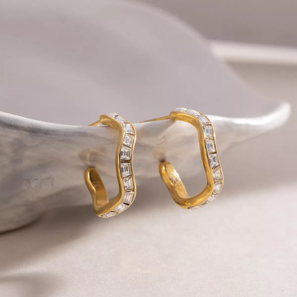 Gold-tone zircon hoop earrings displayed upright on a ceramic dish