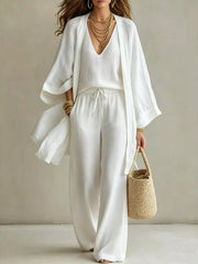 Woman modeling the ivory three-piece set with a handbag, shown full length.