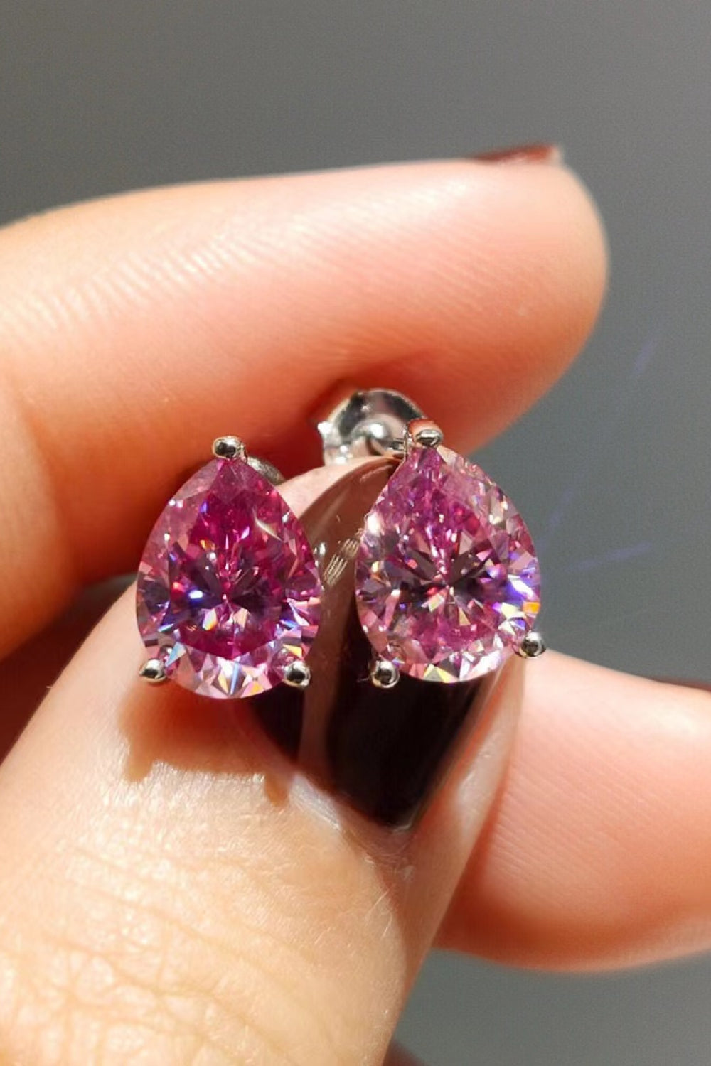 Front view of pink teardrop stud earrings held on a fingertip