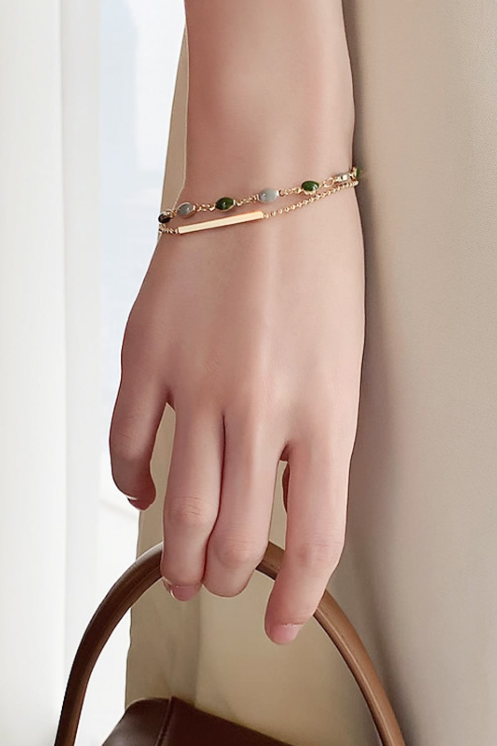 Wrist view of a delicate two-layer gold-tone bracelet with colored stones and slim bar