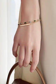 Wrist view of a delicate two-layer gold-tone bracelet with colored stones and slim bar