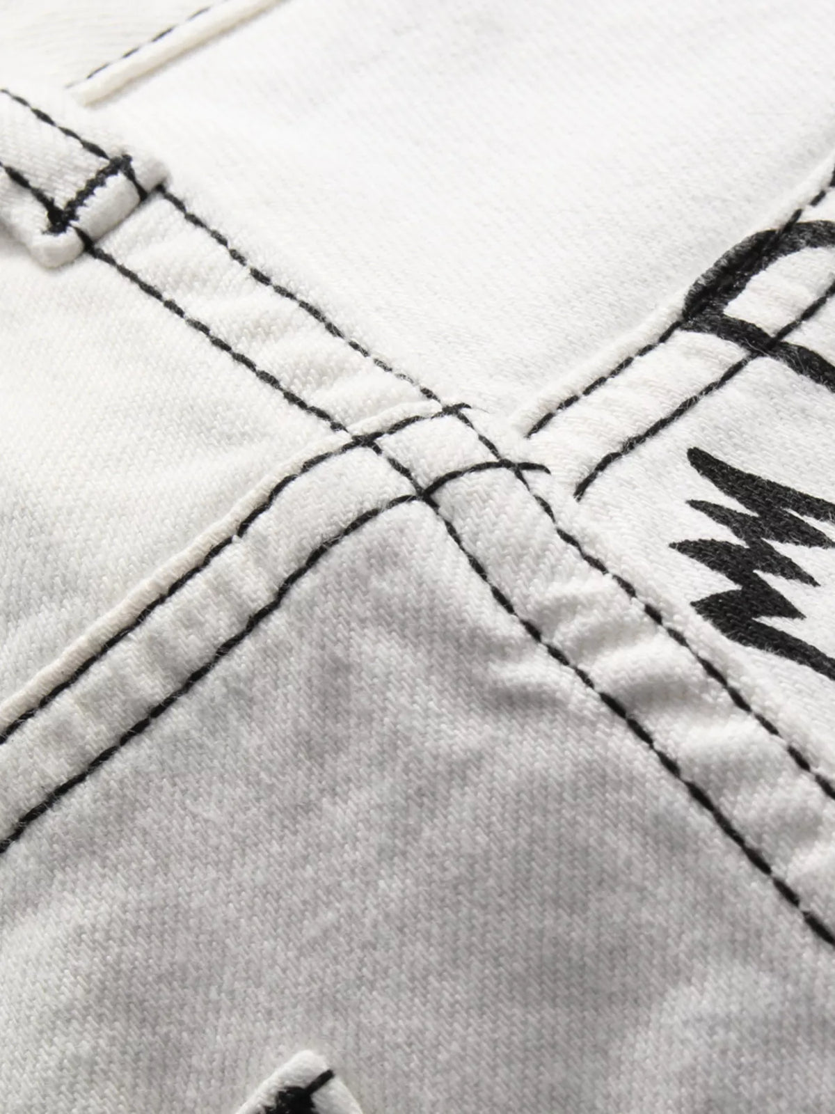 Close-up of double-stitched seam on graffiti-print white jeans