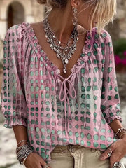 Model wearing pink blouse with green and dark spots, ruffled V-neck and three-quarter sleeves