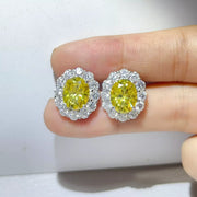 Pair of yellow halo stud earrings shown on a fingertip.