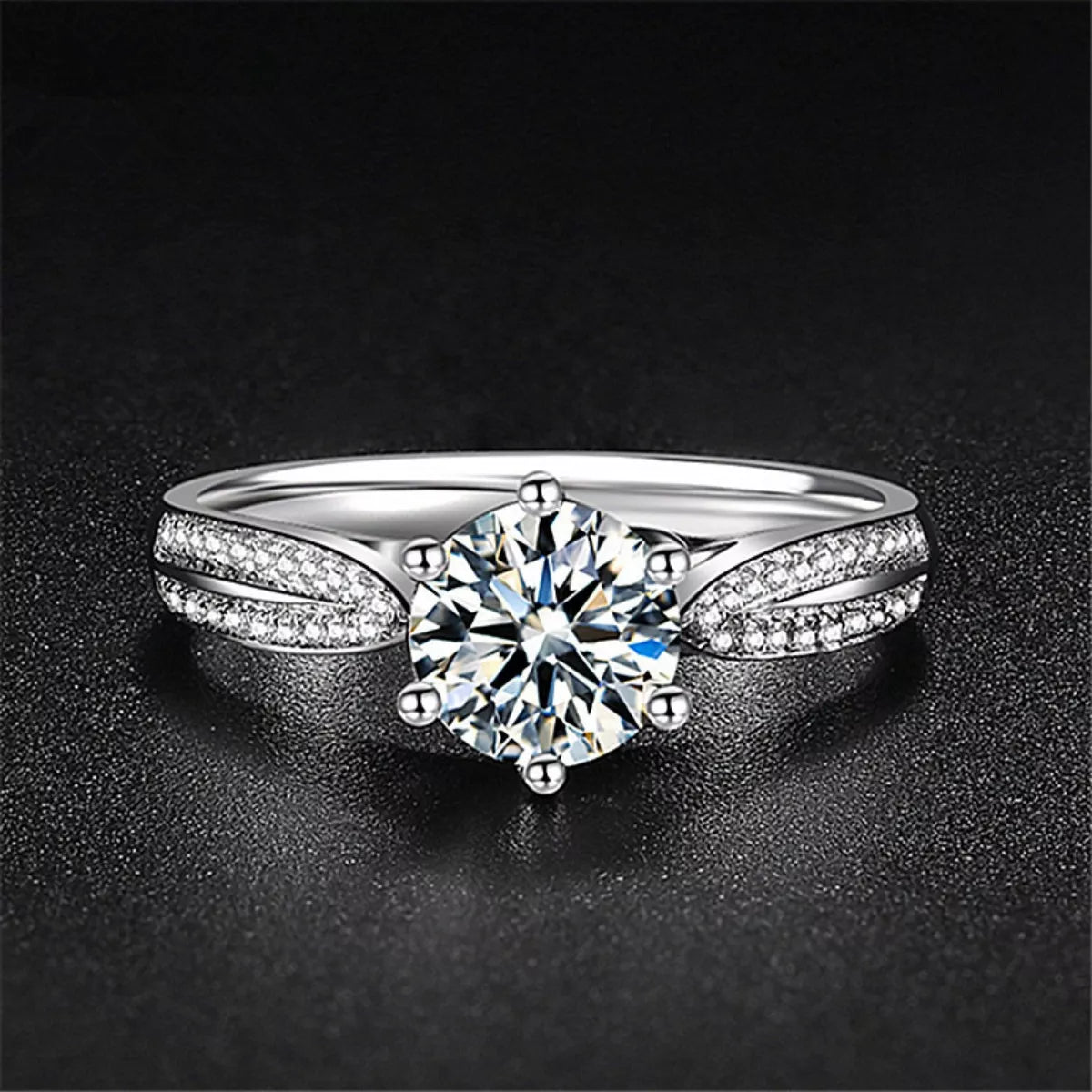 Silver moissanite ring with a round center stone and split pavé-set shoulders on a dark background