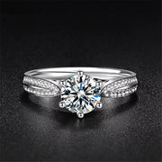 Silver moissanite ring with a round center stone and split pavé-set shoulders on a dark background