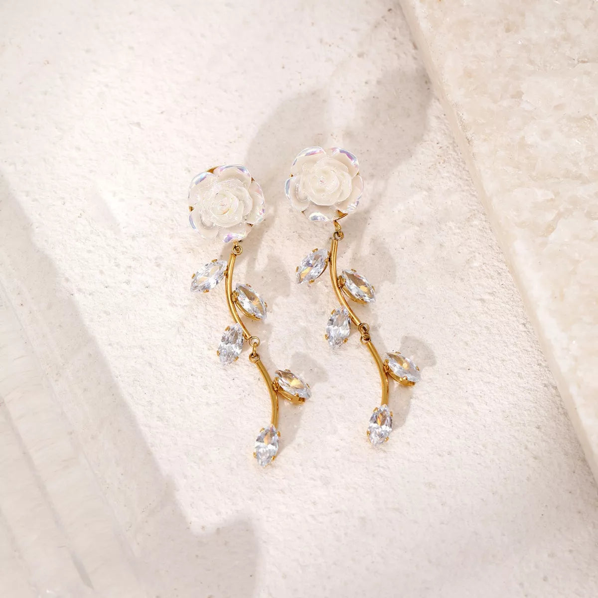 Pair of gold-tone flower drop earrings laid on textured pale fabric