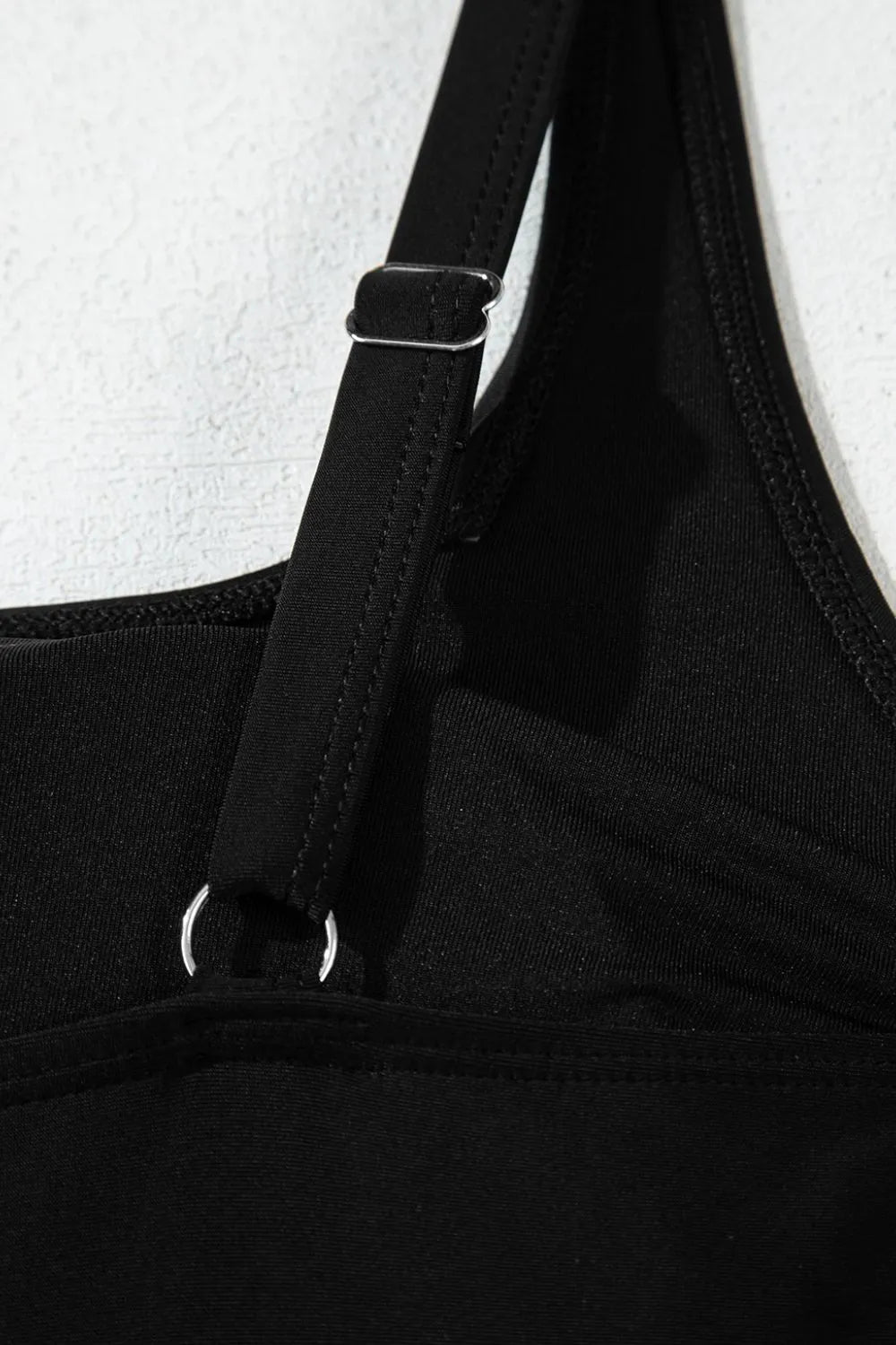 Close detail of the black swim dress shoulder strap adjuster and front seam.