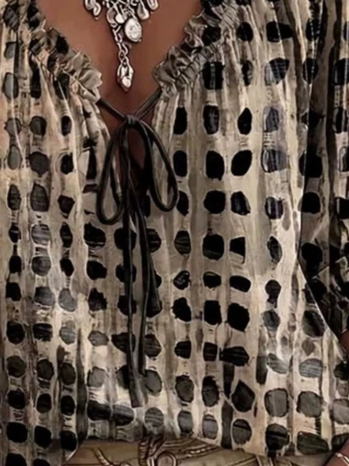 Close-up of beige and black spotted blouse front with ruffled tie neckline