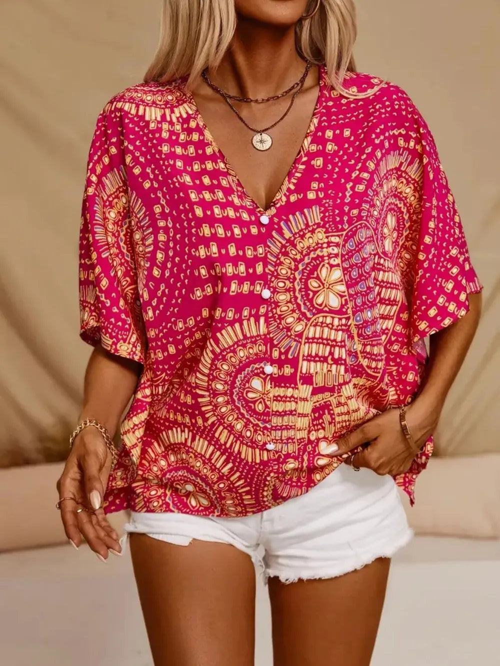 Pink printed blouse on a model with hands at the pockets of white denim shorts.