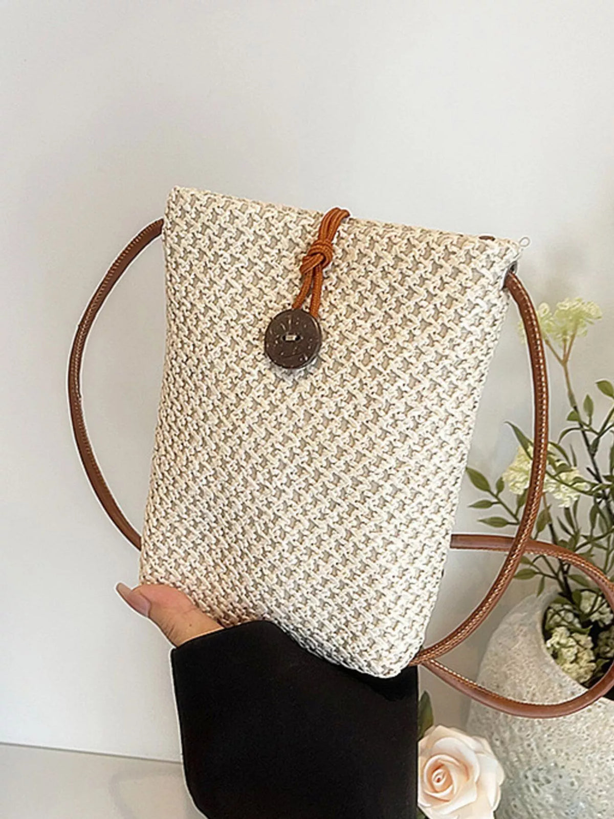 Front view of off-white woven crossbody bag with long brown shoulder strap