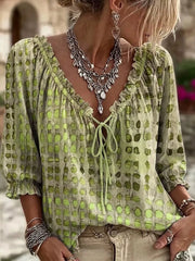 Model wearing a lime green blouse with dark spots and ruffled tie neckline