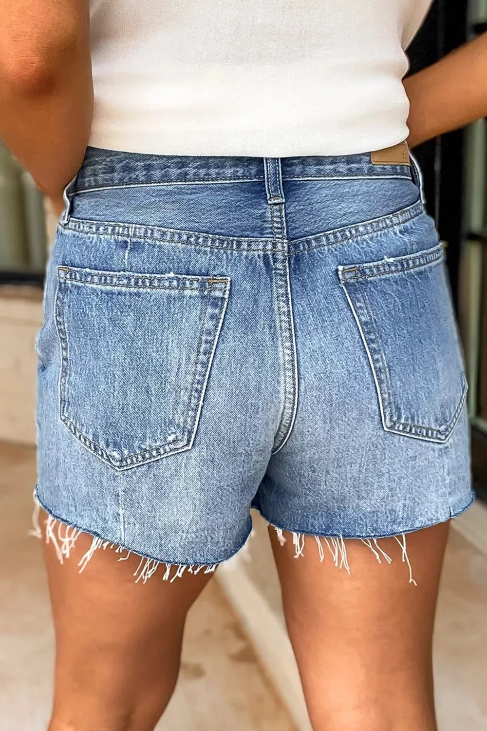 Back view of high-waisted denim shorts with two large patch pockets and frayed hems
