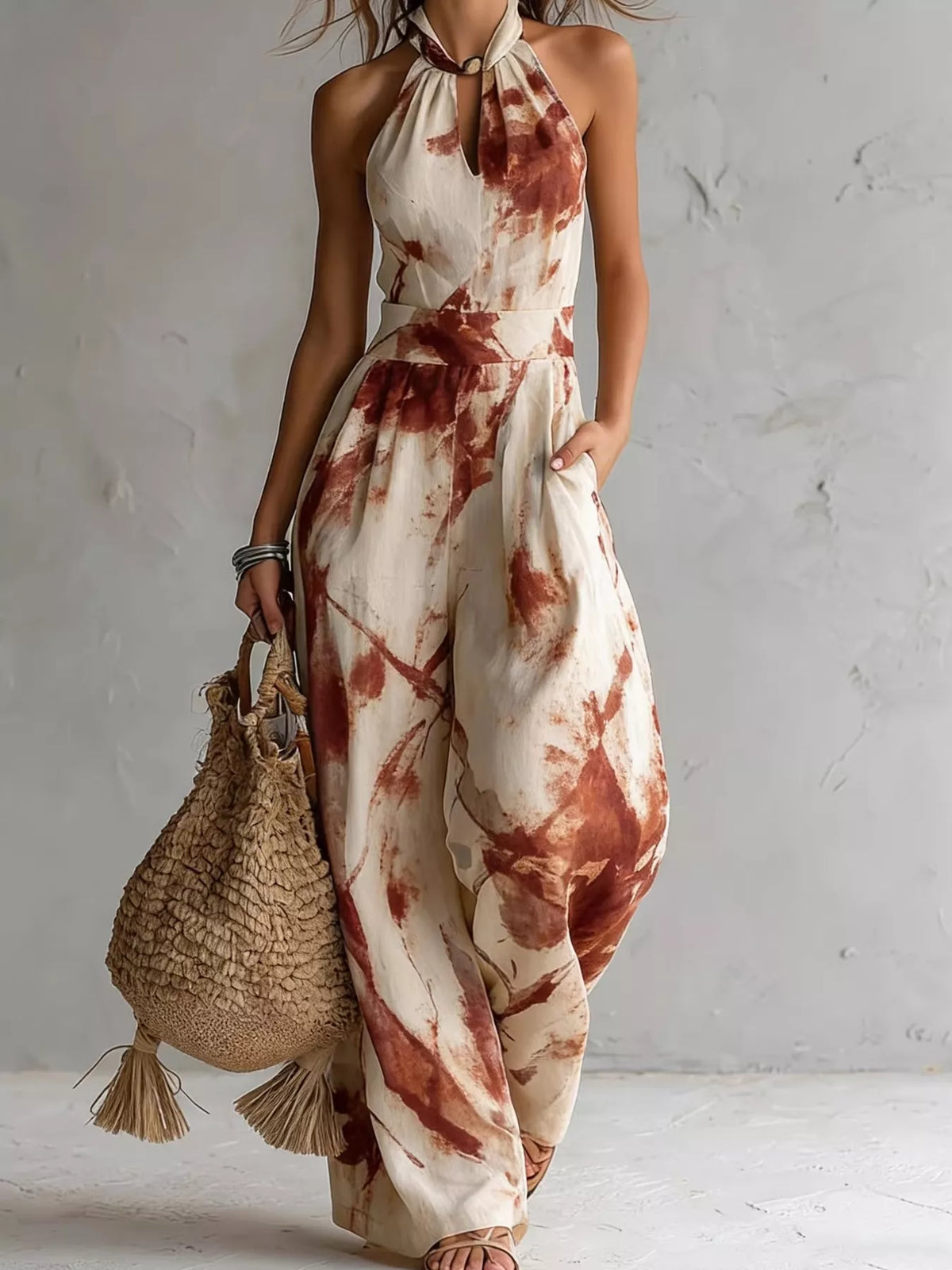 Cream jumpsuit with rust-red ink-wash print, full-length front view with a woven bag.