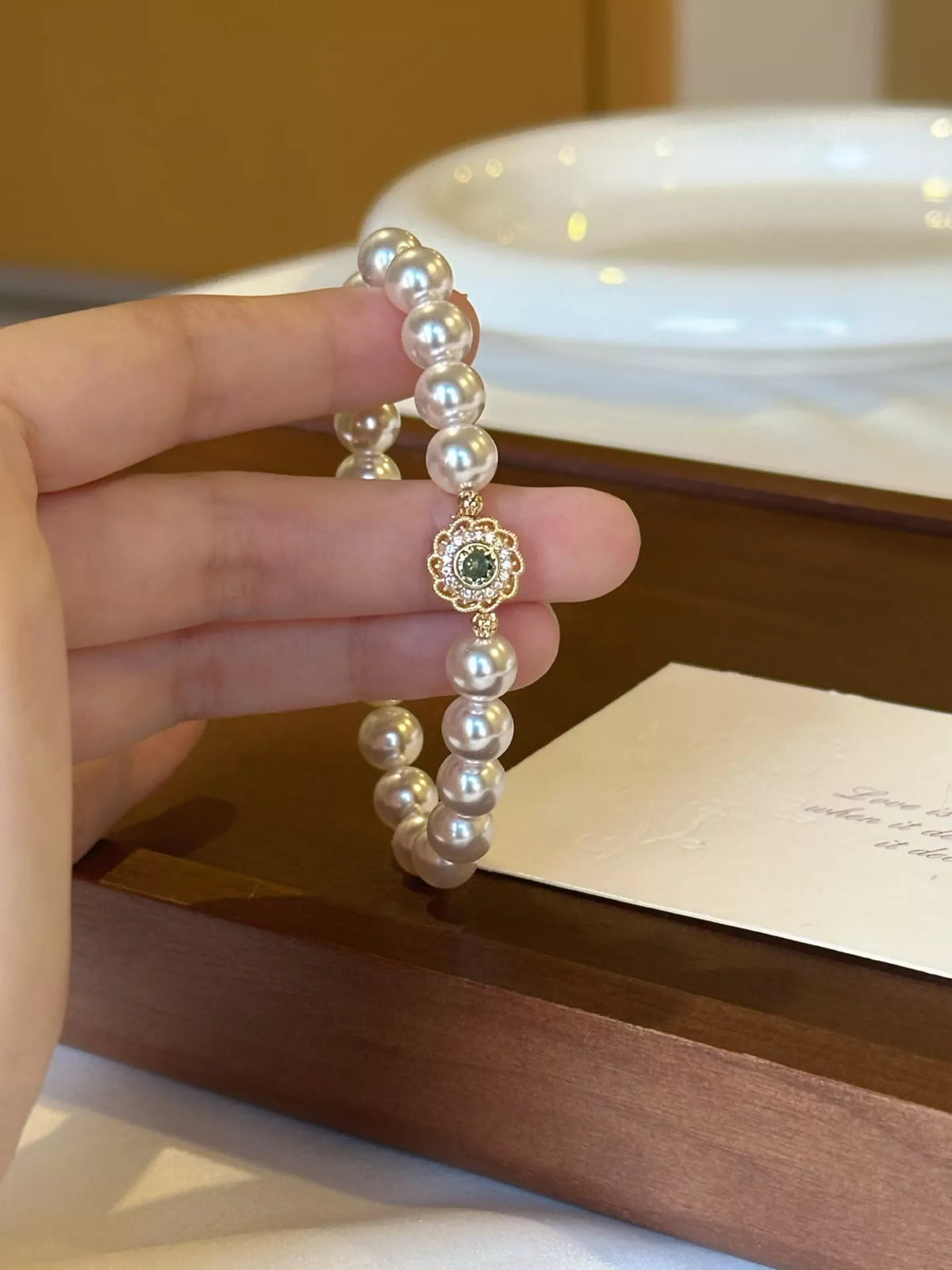 Pearl bracelet with a small gold floral charm held upright between fingers