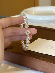Pearl bracelet with a small gold floral charm held upright between fingers
