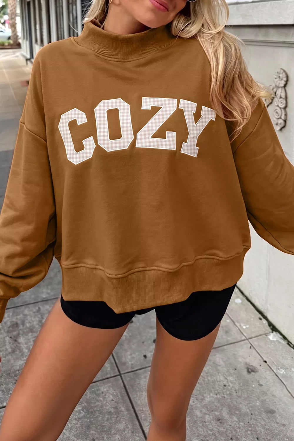 Close view of white COZY lettering on brown sweatshirt